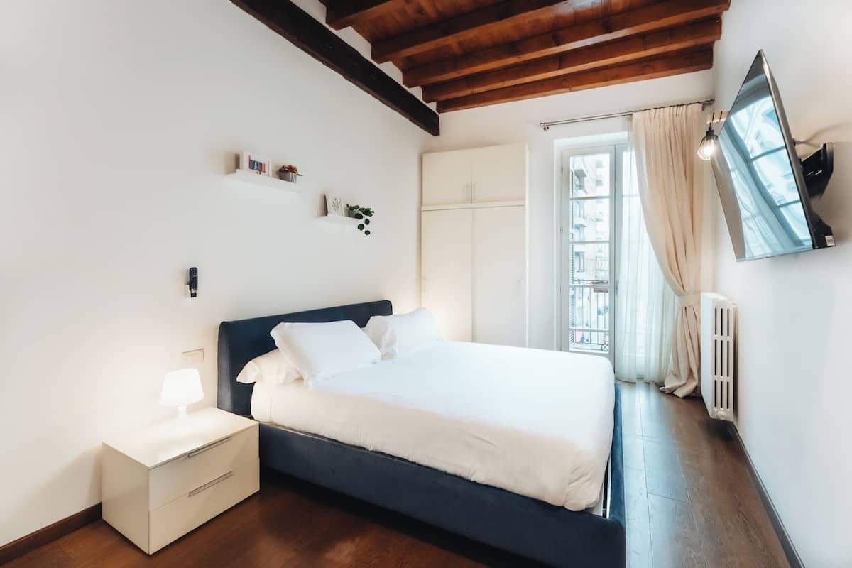 A bedroom with a bed, nightstand, and a mounted TV.