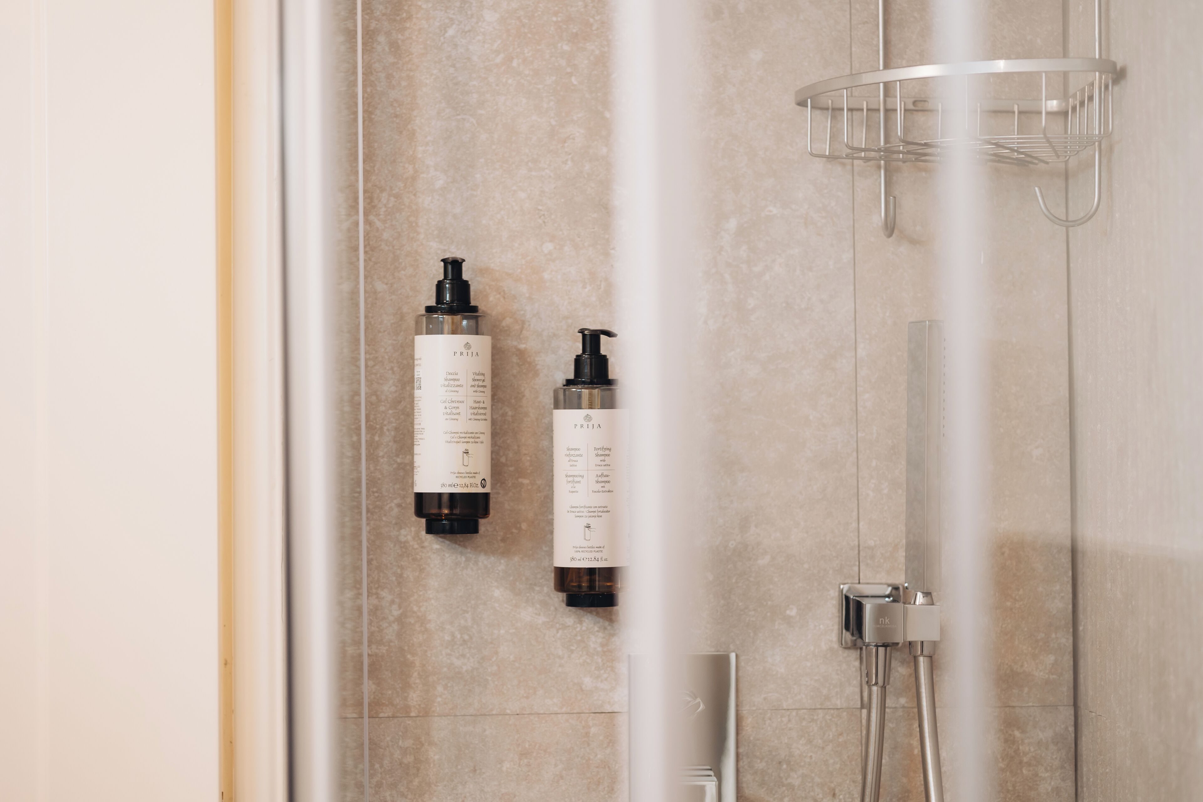 A shower area with a glass door, a metal showerhead, and two bottles of shampoo on the wall.