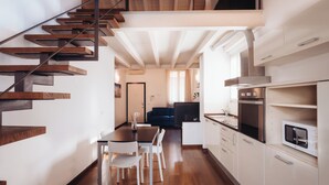 A modern kitchen with white cabinets, a wooden staircase, and a dining area with a table and chairs. - La dimora di Brera (Milan)