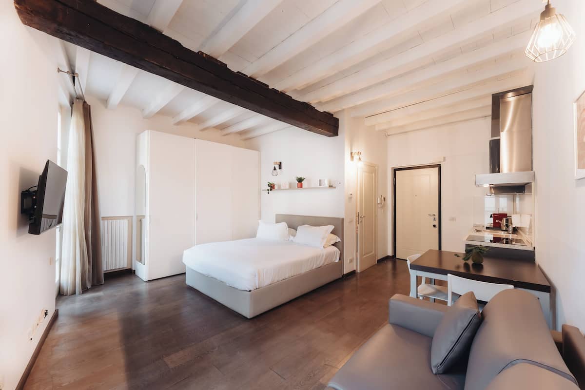 A bedroom with a bed, a sofa, a desk, and a kitchenette.