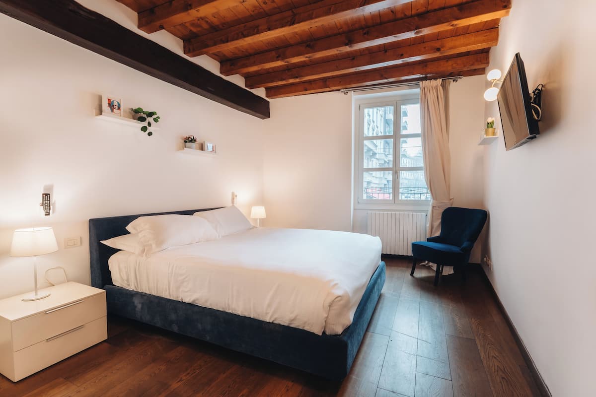A bedroom with a bed, bedside table, lamp, and a chair.