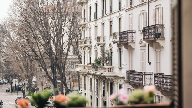 A street view with a row of white buildings, balconies, and a tree in the foreground. - La dimora di Brera (Milan)