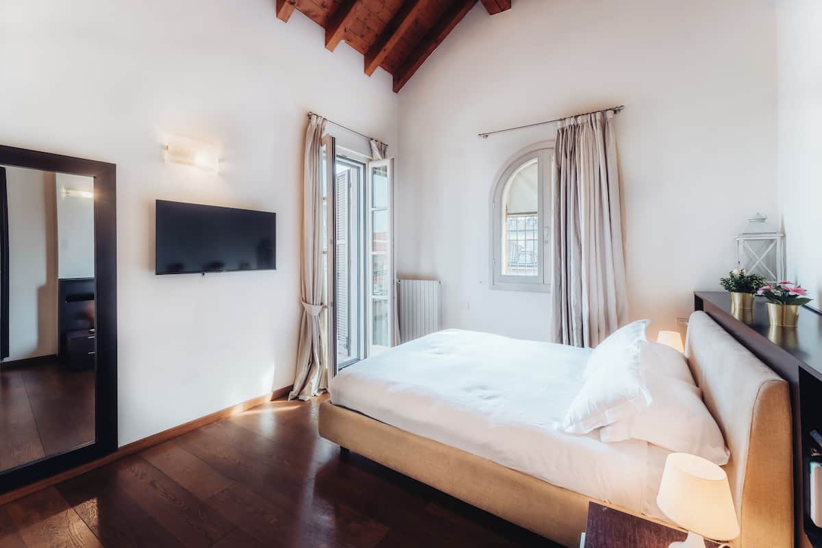 A bedroom with a bed, a TV mounted on the wall, and a window with curtains.