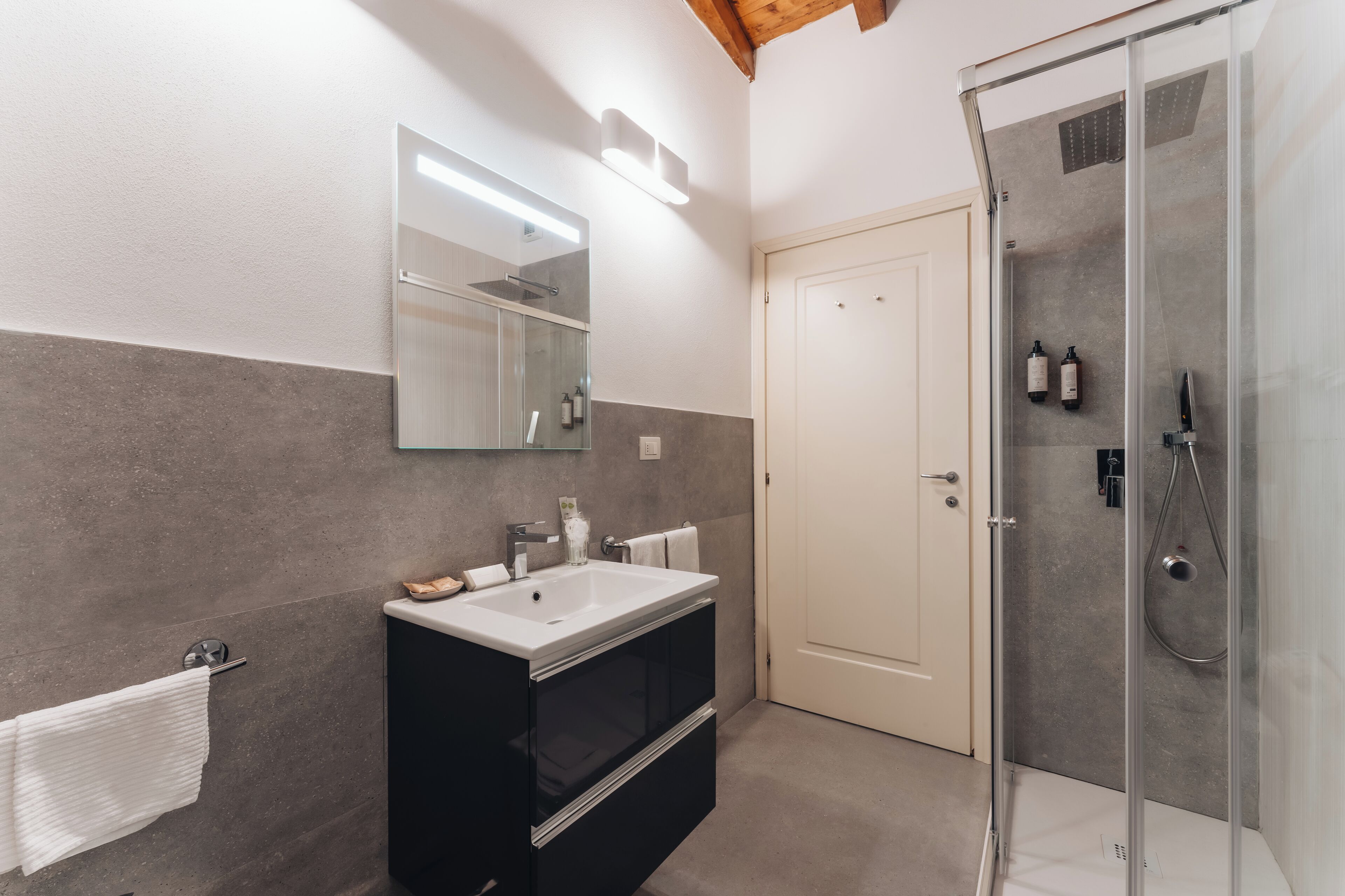 A modern bathroom with a glass-enclosed shower, a large mirror, and a dark-toned vanity.