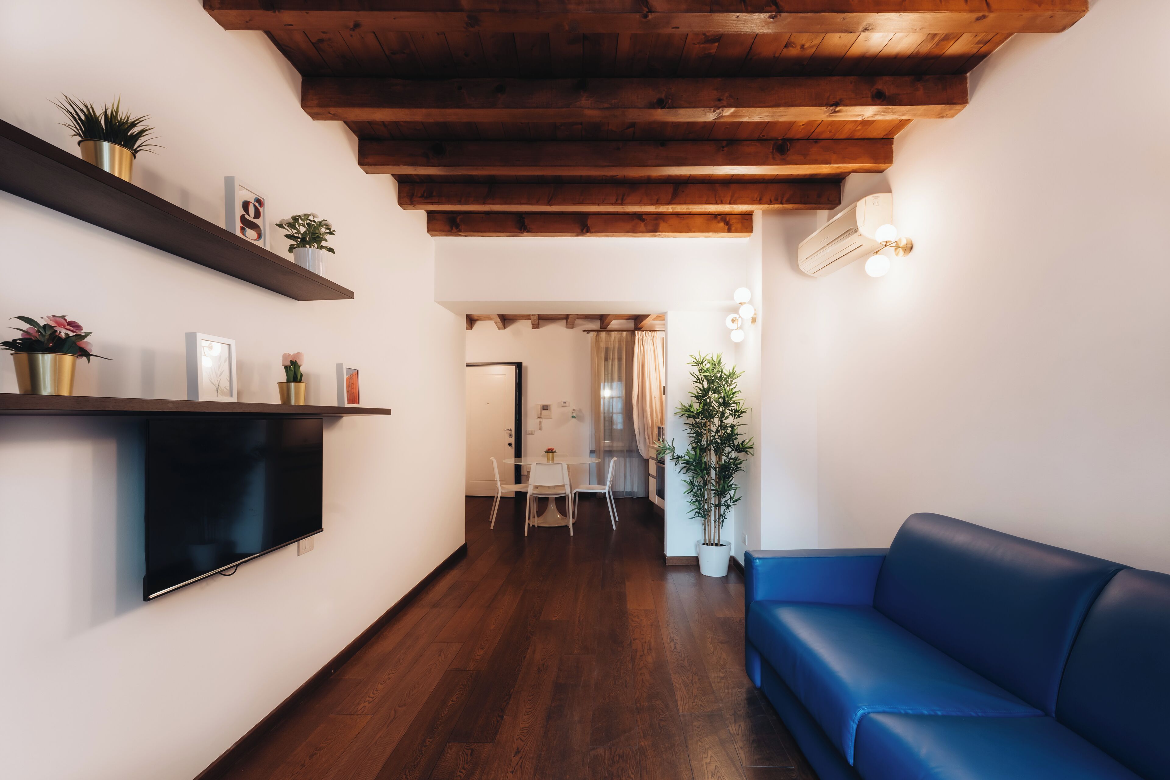 Een moderne woonkamer met een houten plafond, een blauwe bank, een flatscreen-tv en een eethoek met een tafel en stoelen.
