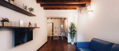 Een moderne woonkamer met een houten plafond, een blauwe bank, een flatscreen-tv en een eethoek met een tafel en stoelen.