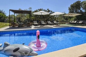 Una piscina con tumbonas y sombrillas, rodeada de vegetación.