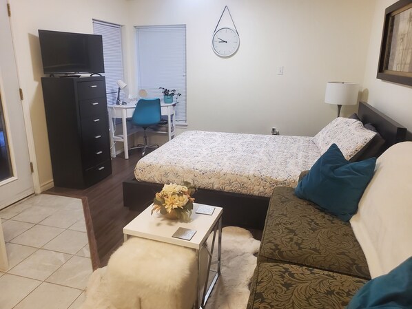 A bedroom with a bed, a desk, a chair, a TV, and a clock on the wall.