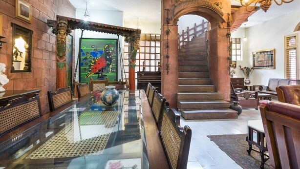 A spacious lobby with a glass-top dining table, a staircase, and traditional decor. - Hotel Malhar Haveli (Noida)