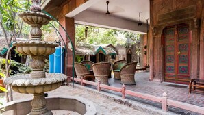 A courtyard with a stone fountain, wicker furniture, and a traditional door. - Hotel Malhar Haveli (Noida)