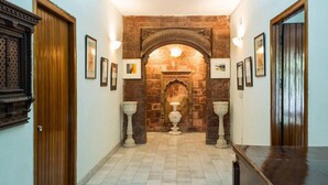 A hallway with a stone archway, framed artwork, and a tiled floor. - Hotel Malhar Haveli (Noida)
