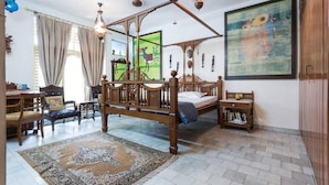 A spacious bedroom with a four-poster bed, a small bedside table, a rug, and a painting on the wall. - Hotel Malhar Haveli (Noida)