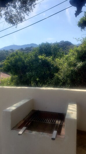 A balcony with a grill, overlooking a mountainous landscape with dense greenery.