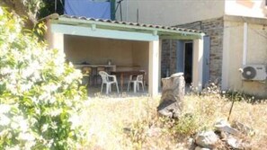 Un espace extérieur abrité, équipé d’une table et de chaises, d’un mur en pierre et d’un appareil de climatisation.