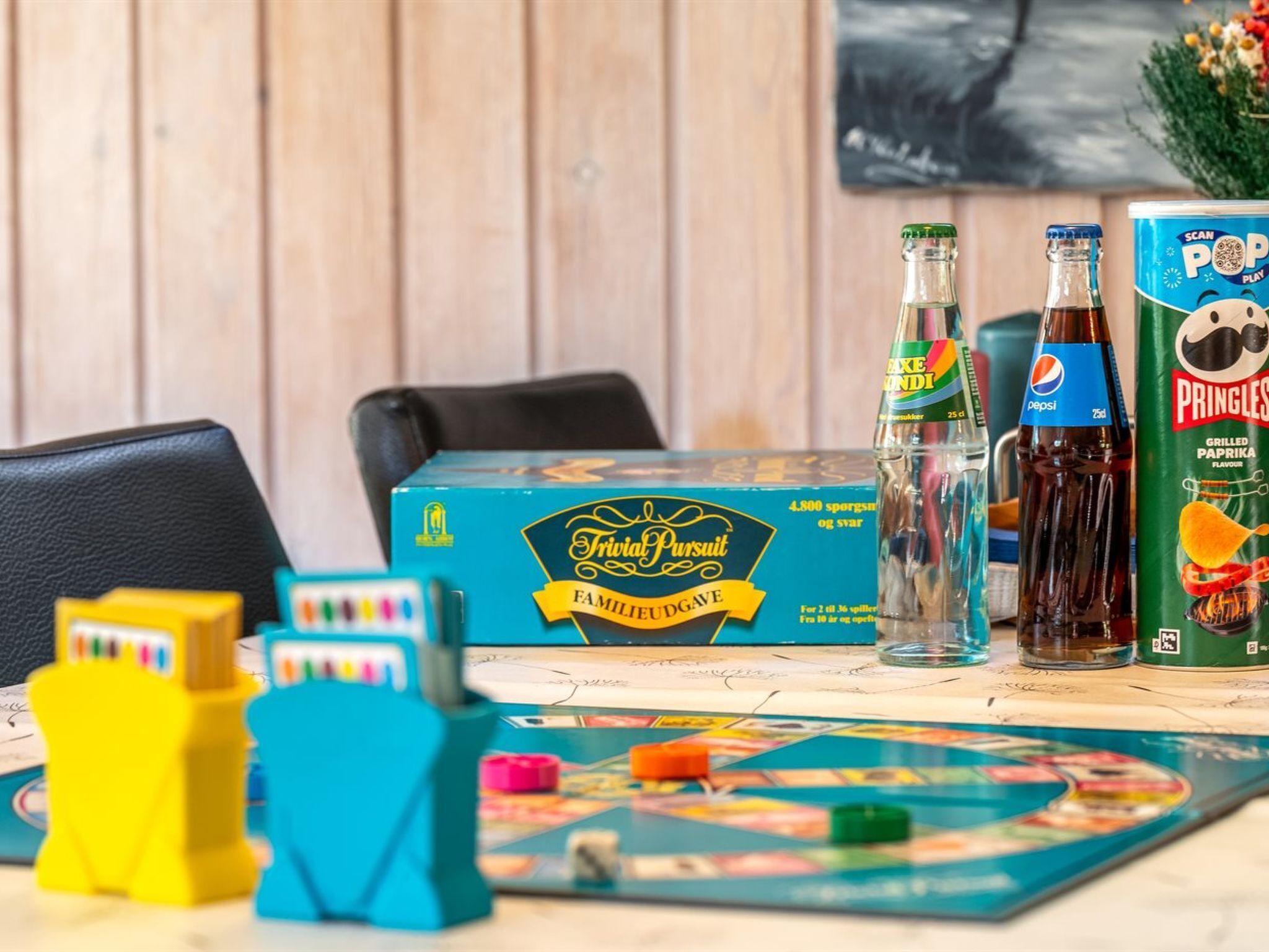 A board game, a bottle of beer, a Pepsi bottle, and a Pringles can on a table.