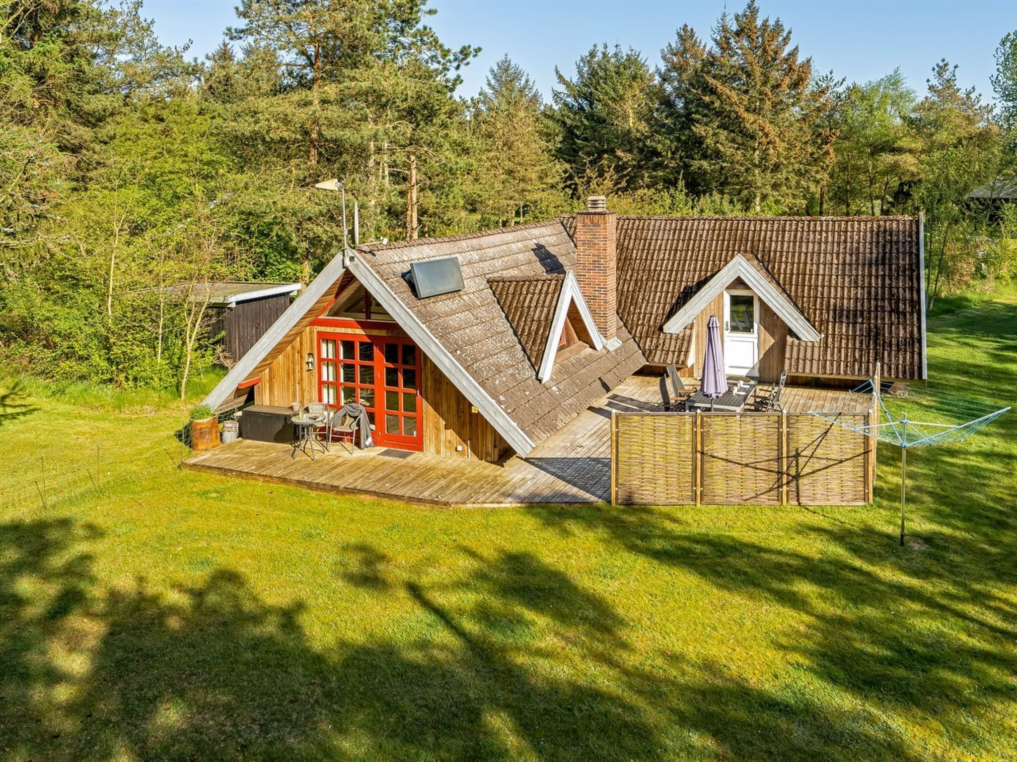 Eine Holzhütte mit geneigtem Dach, einer Terrasse und einer kleinen Sitzgelegenheit im Freien.