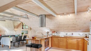 A modern kitchen with wooden cabinets, a stainless steel range hood, and a dining area with a table and chairs. - "Niesina" - 600m to the fjord by Interhome (Højslev)