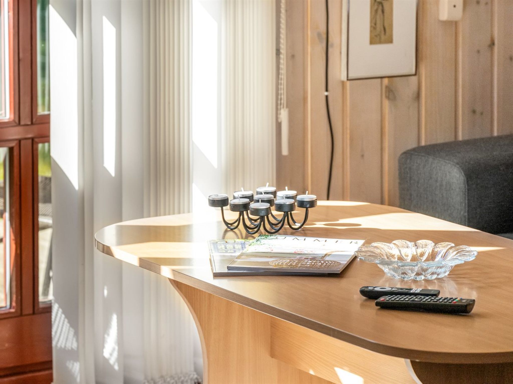 A wooden table with a candle holder, a remote control, and a glass bowl.