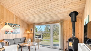 L’intérieur d’un chalet accueillant, avec un plafond en bois, un canapé, une table, une cheminée et une grande fenêtre.