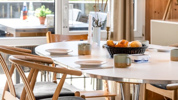 Une table de salle à manger ronde, entourée de chaises, un panier de pain, une tasse et un chandelier.