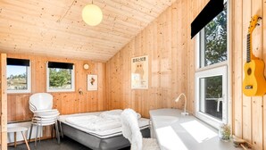 Une cabane confortable avec un lit, un bureau, une chaise, une guitare et une fenêtre donnant sur la forêt.