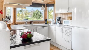 Une cuisine moderne avec des meubles blancs, un plan de travail noir et une grande fenêtre donnant sur la verdure.