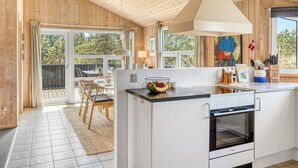 Une cuisine moderne dotée d’un îlot central, d’un coin repas avec des chaises et offrant une vue sur l’extérieur grâce à de grandes fenêtres.