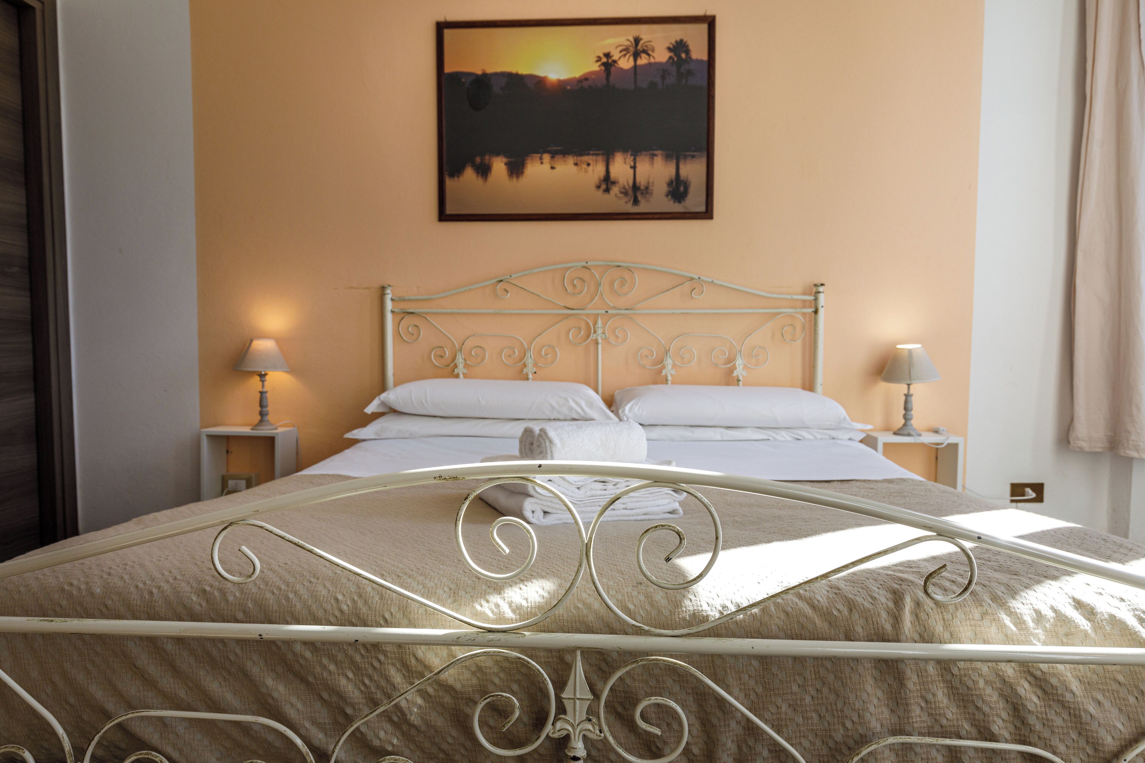 A neatly made bed with white linens, a metal headboard, and two bedside lamps.