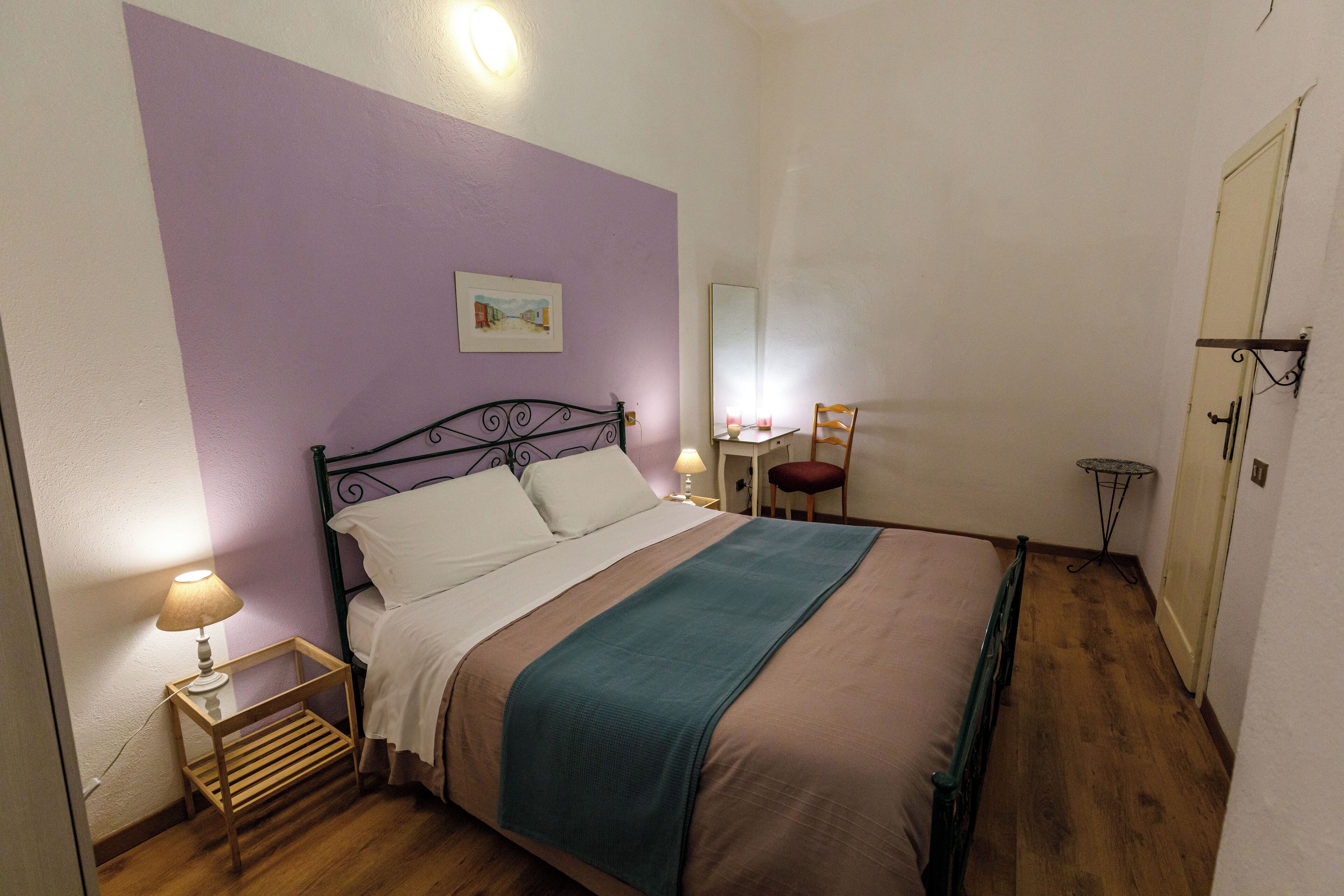 A bedroom with a bed, bedside table, lamp, and a small table with a mirror.
