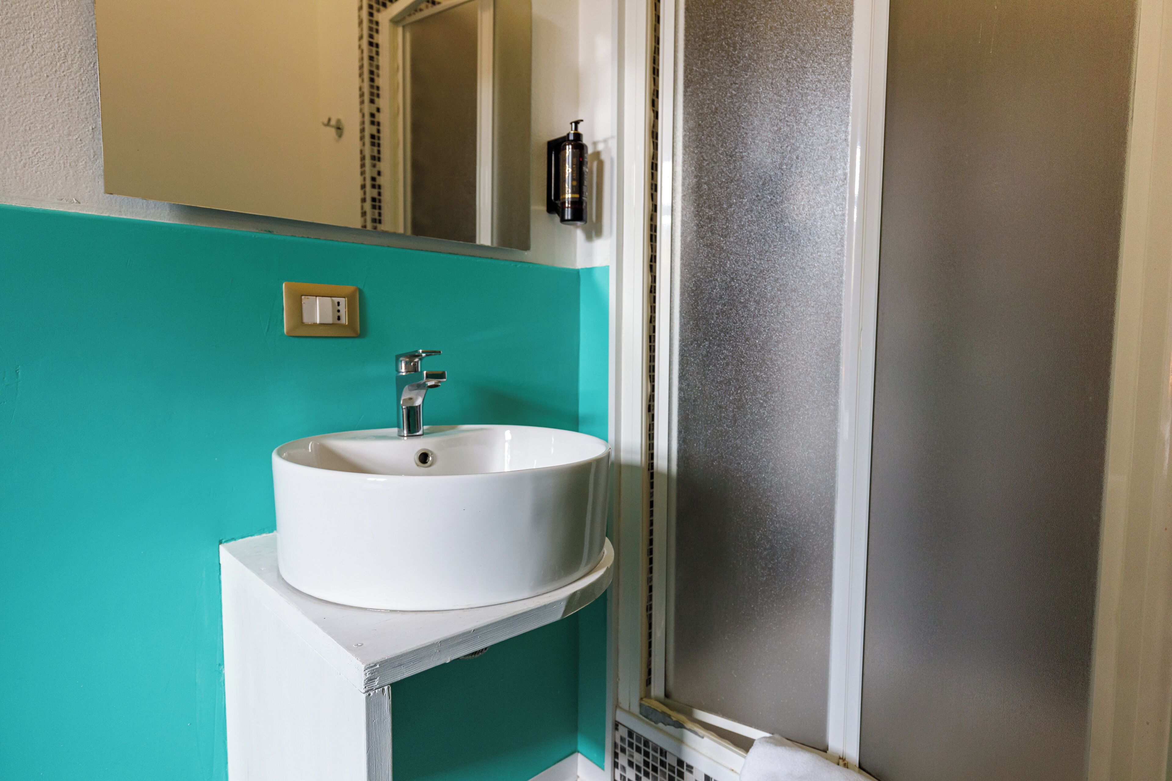 A bathroom with a white sink, a mirror, and a frosted glass shower enclosure.