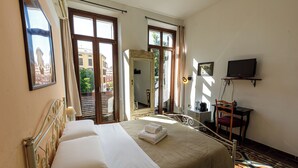 Ein Hotelzimmer mit Bett, Schreibtisch, Stuhl, Fernseher und einem Fenster mit Blick auf Gebäude.