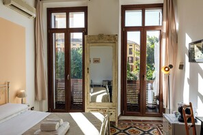 Un dormitori amb un llit, un mirall gran, un escriptori i vista a edificis per les finestres.