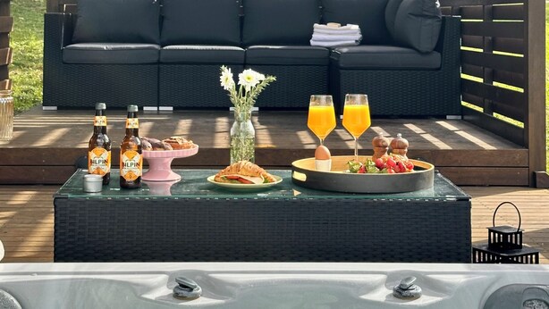 Un patio con un jacuzzi, un sofá, una mesa con bebidas y aperitivos.