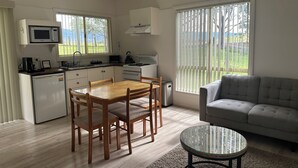Cocina compacta con microondas, estufa y lavaplatos. Hay una mesa de comedor con sillas y un sofá en la sala.