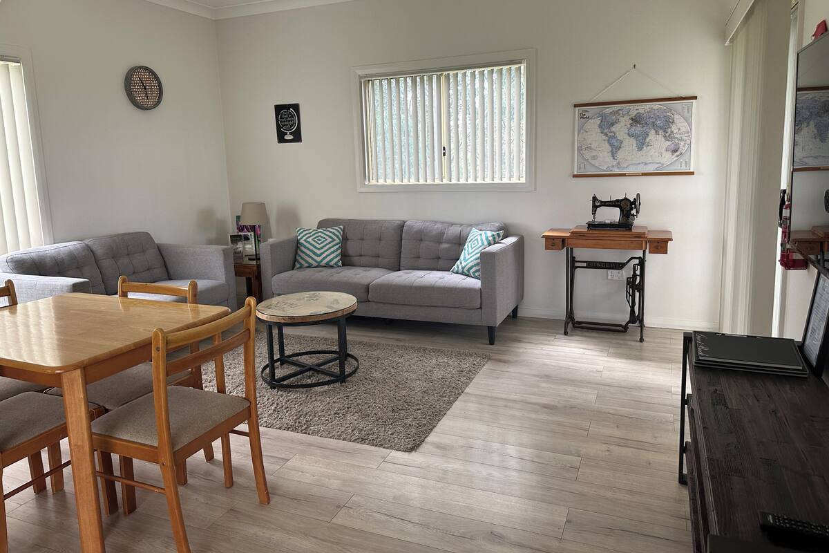 Una sala de estar con un sofá gris, una mesa de centro redonda y una mesa de comedor de madera con sillas.