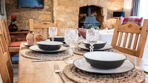 A wooden dining table set with black plates, clear glassware, and a woven placemat. - Quaint and traditional dog friendly - Archway Cottage (Blockley)