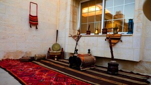 A traditional room with a patterned carpet, a window with decorative items, and a wall-mounted shelf with various objects. - JORDAN VIEW HOTEL (Amman)