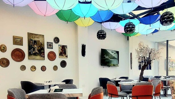 A room with a ceiling adorned with colorful umbrellas, a wall with various framed pictures and coins, and a seating area with checkered and solid-colored chairs. - JORDAN VIEW HOTEL (Amman)