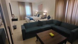A hotel room with a sofa, a wooden coffee table, a bed with a blue blanket, and two bedside lamps. - JORDAN VIEW HOTEL (Amman)