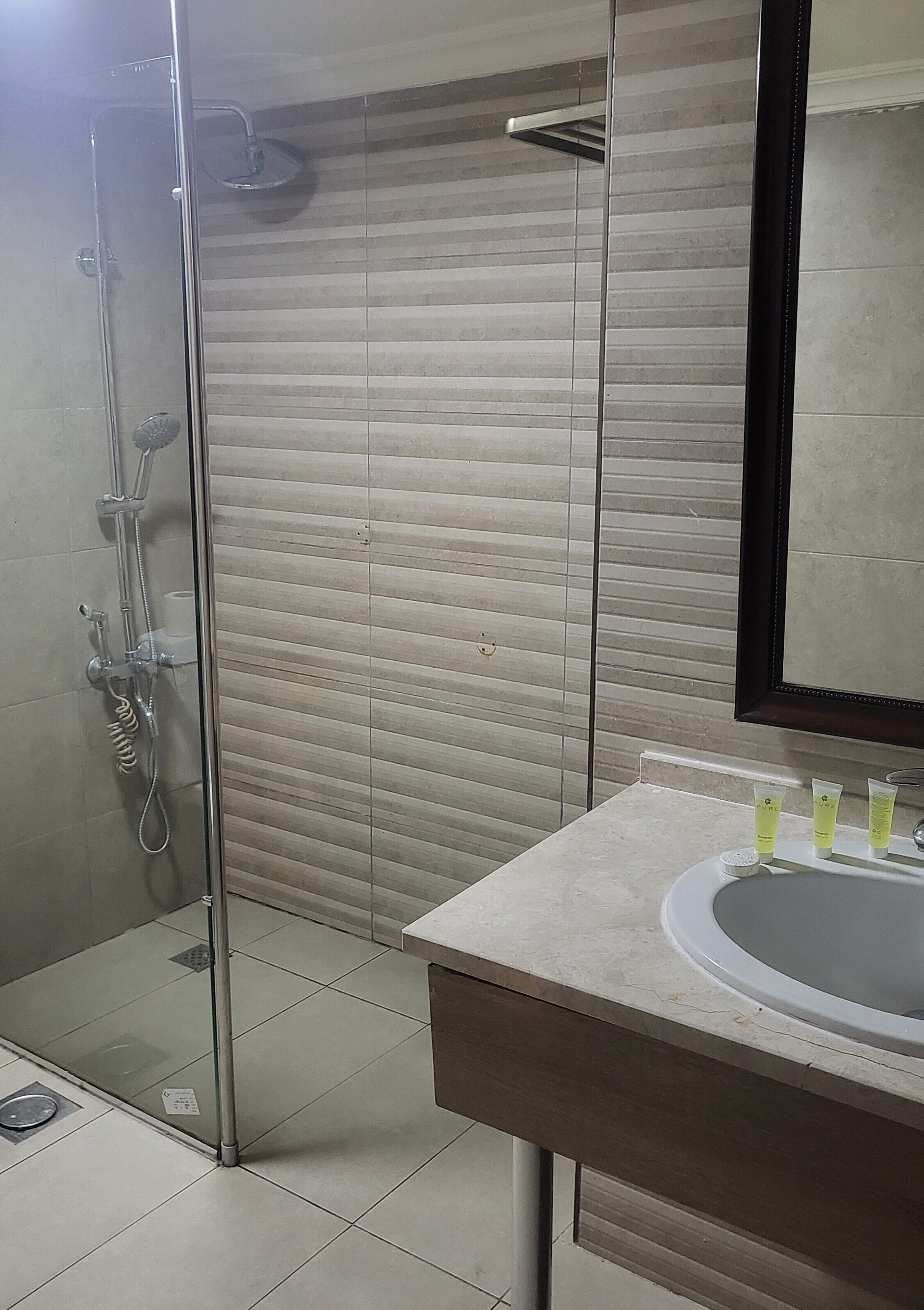 Uma casa de banho moderna com cabine de duche em vidro, um espelho grande e lavatório com artigos de higiene.
