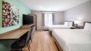 A hotel room with a wooden desk, a television, two beds, and a window with curtains.
