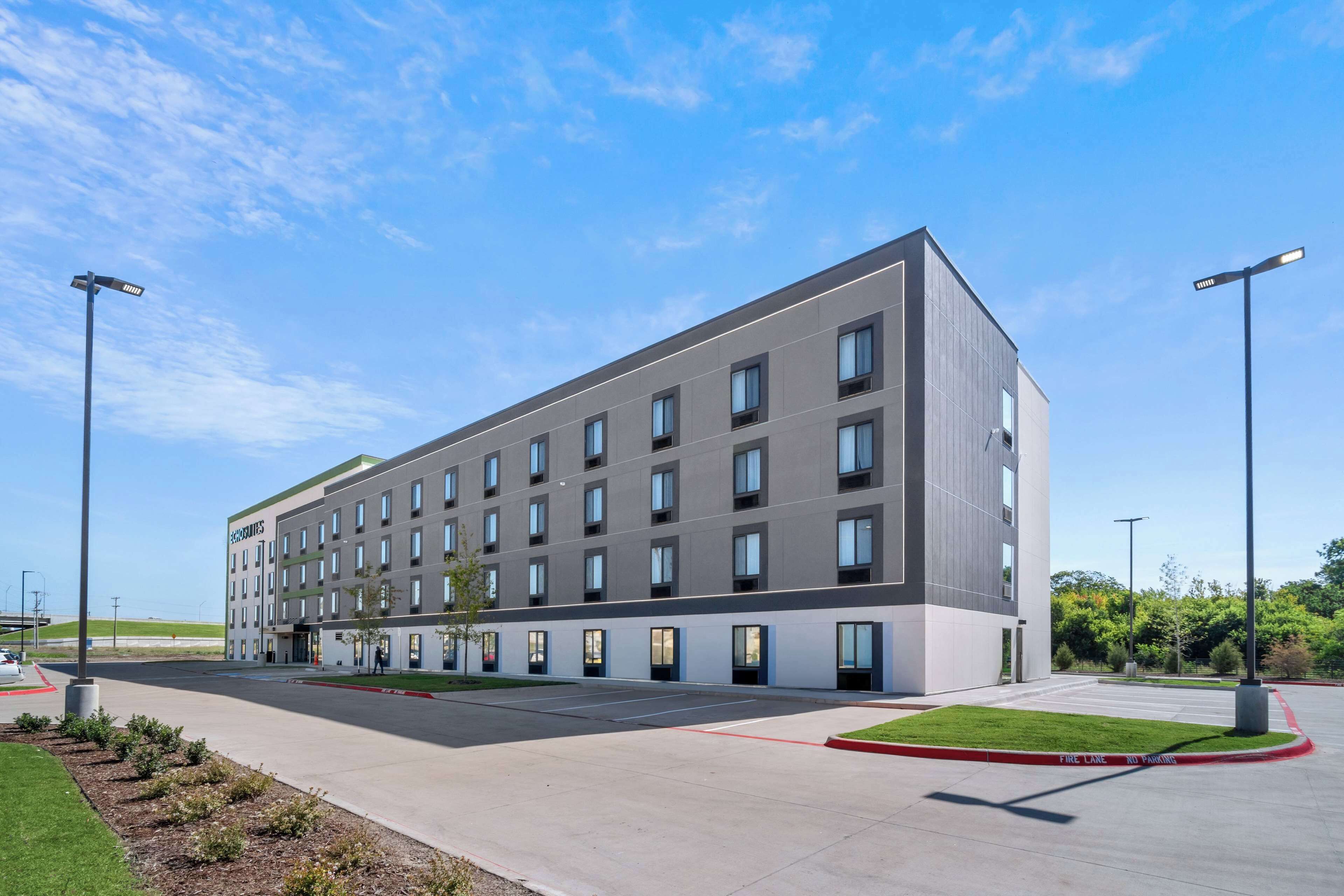 A modern hotel building with a flat facade, multiple windows, and a parking area with a red curb.