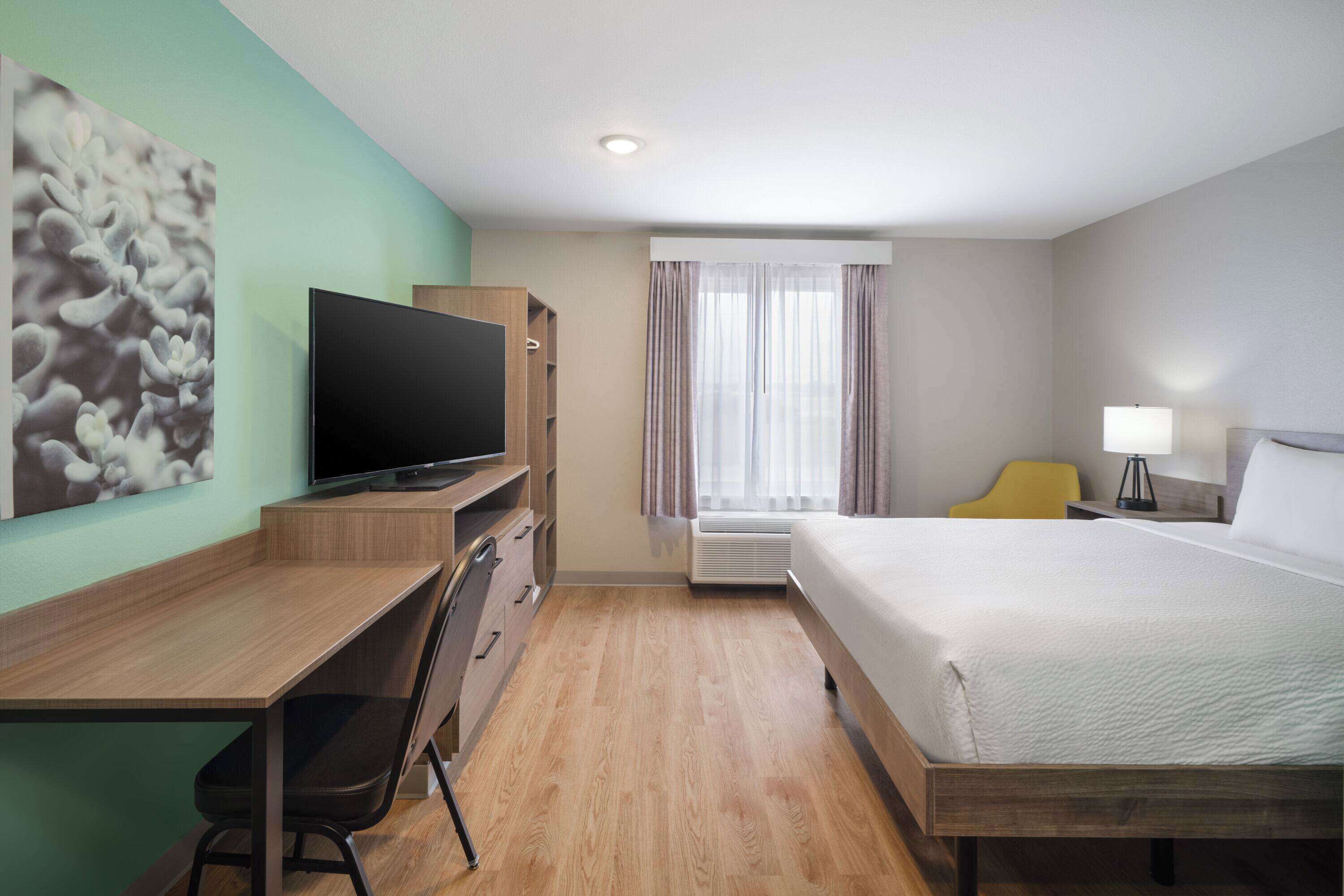 Una habitación de hotel con una cama, un escritorio con una silla, un televisor, una lámpara y una ventana con cortinas.