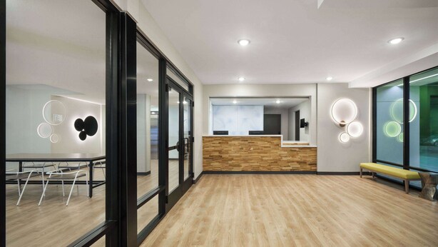 A modern office space with a reception desk, wooden flooring, glass walls, and a bench.