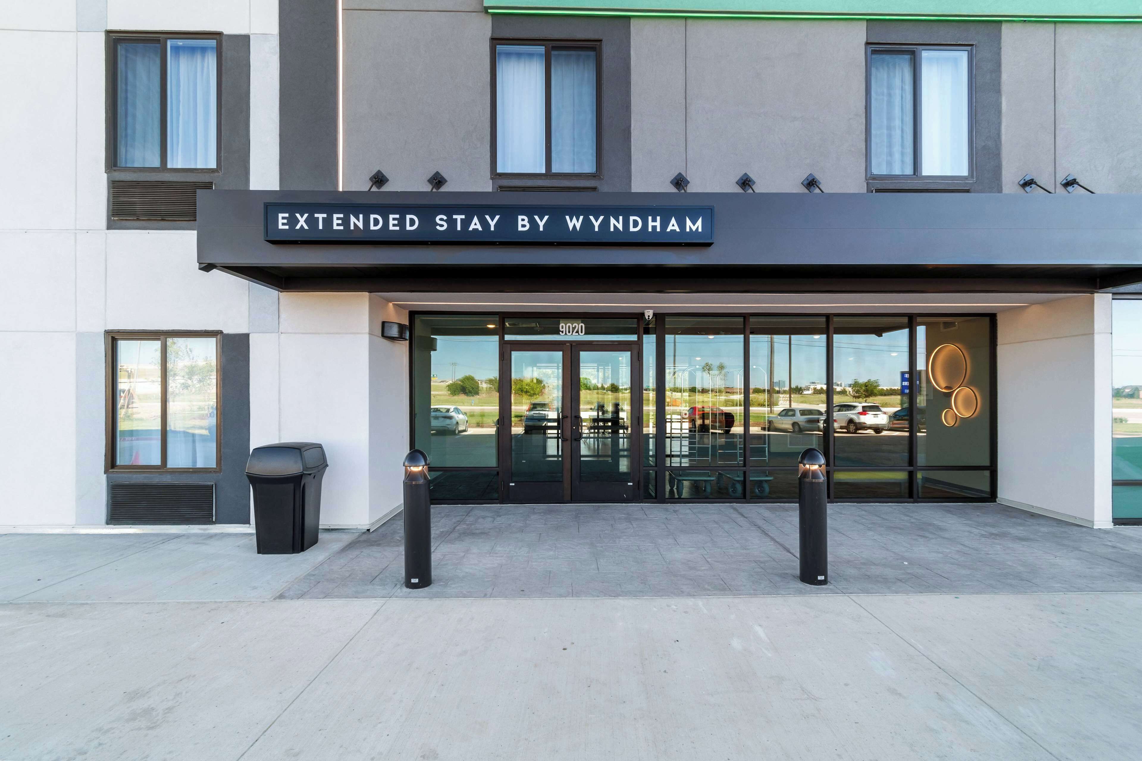 The exterior of a hotel named 'Extended Stay by Wyndham' with a modern facade, large glass entrance, and a parking lot visible in the background.