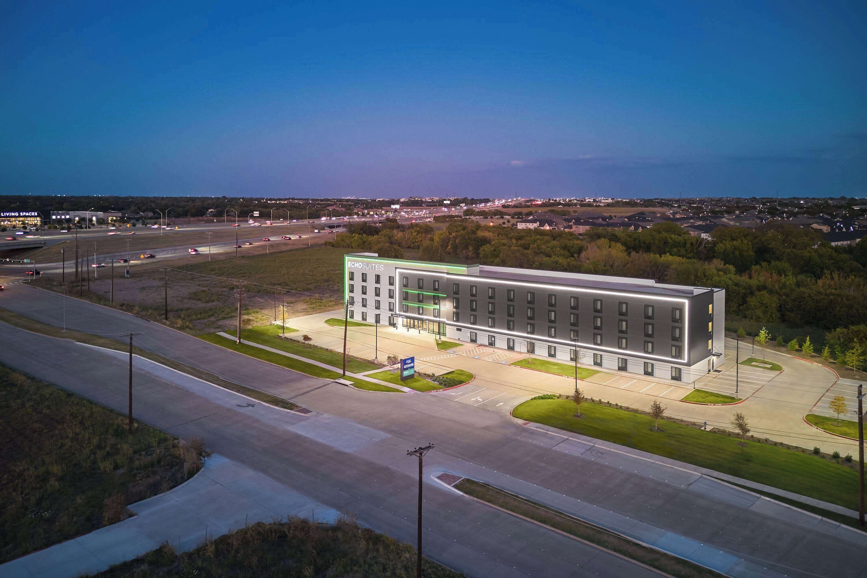 A modern hotel with a central courtyard, multiple floors, and a parking lot.