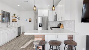 A modern kitchen with white cabinetry, a large island with stools, stainless steel appliances, and pendant lighting. - Charming House & Cottage in Downtown Phoenix (Phoenix)