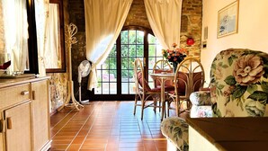 A cozy room with a wooden dining table, chairs, and a floral sofa. A large window with curtains allows natural light to fill the space. - Tuscan Comfort in Varna (Montaione)