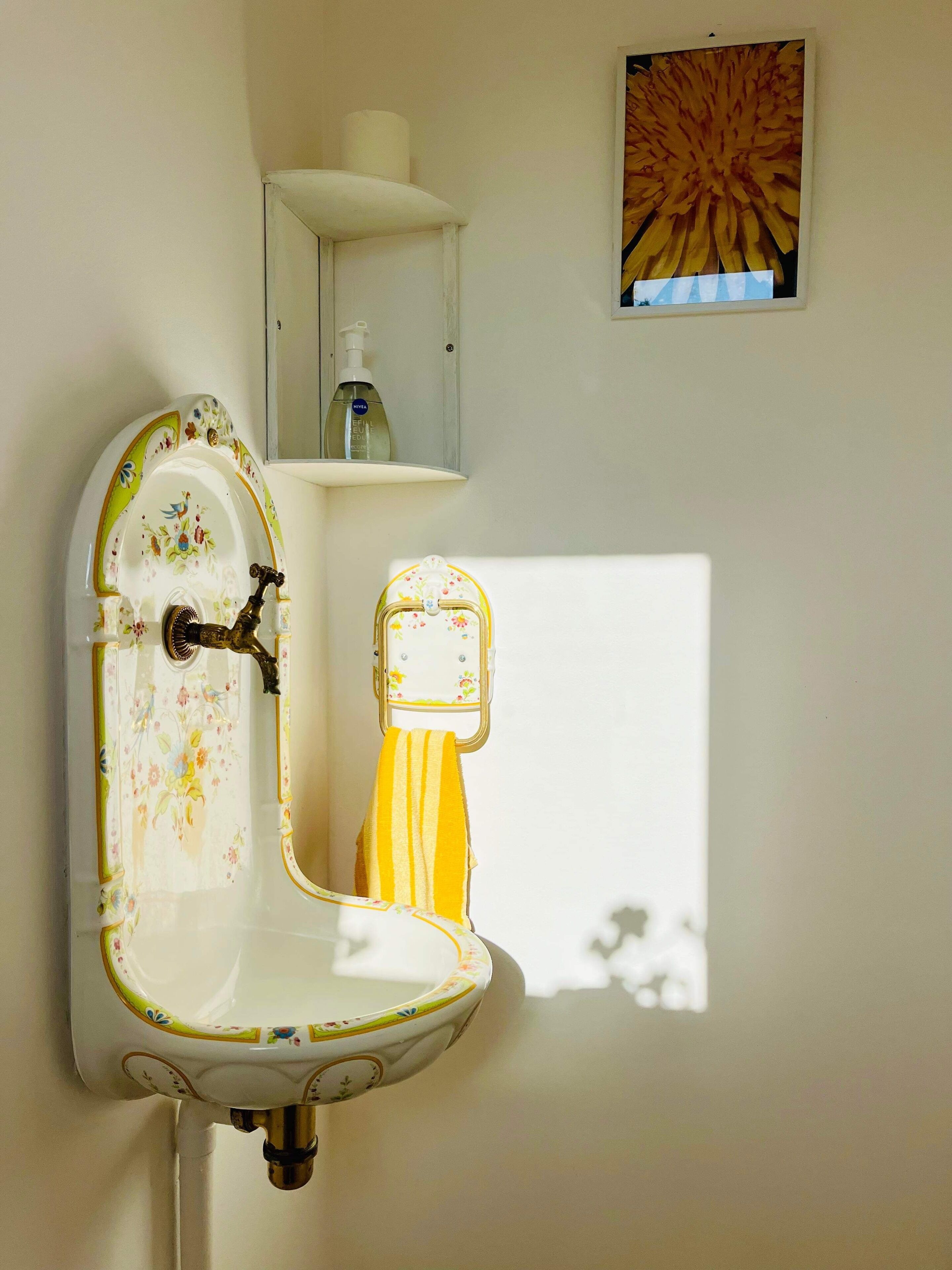 A vintage-style sink with floral patterns, a yellow towel hanging on it, and a small shelf with a soap dispenser above.