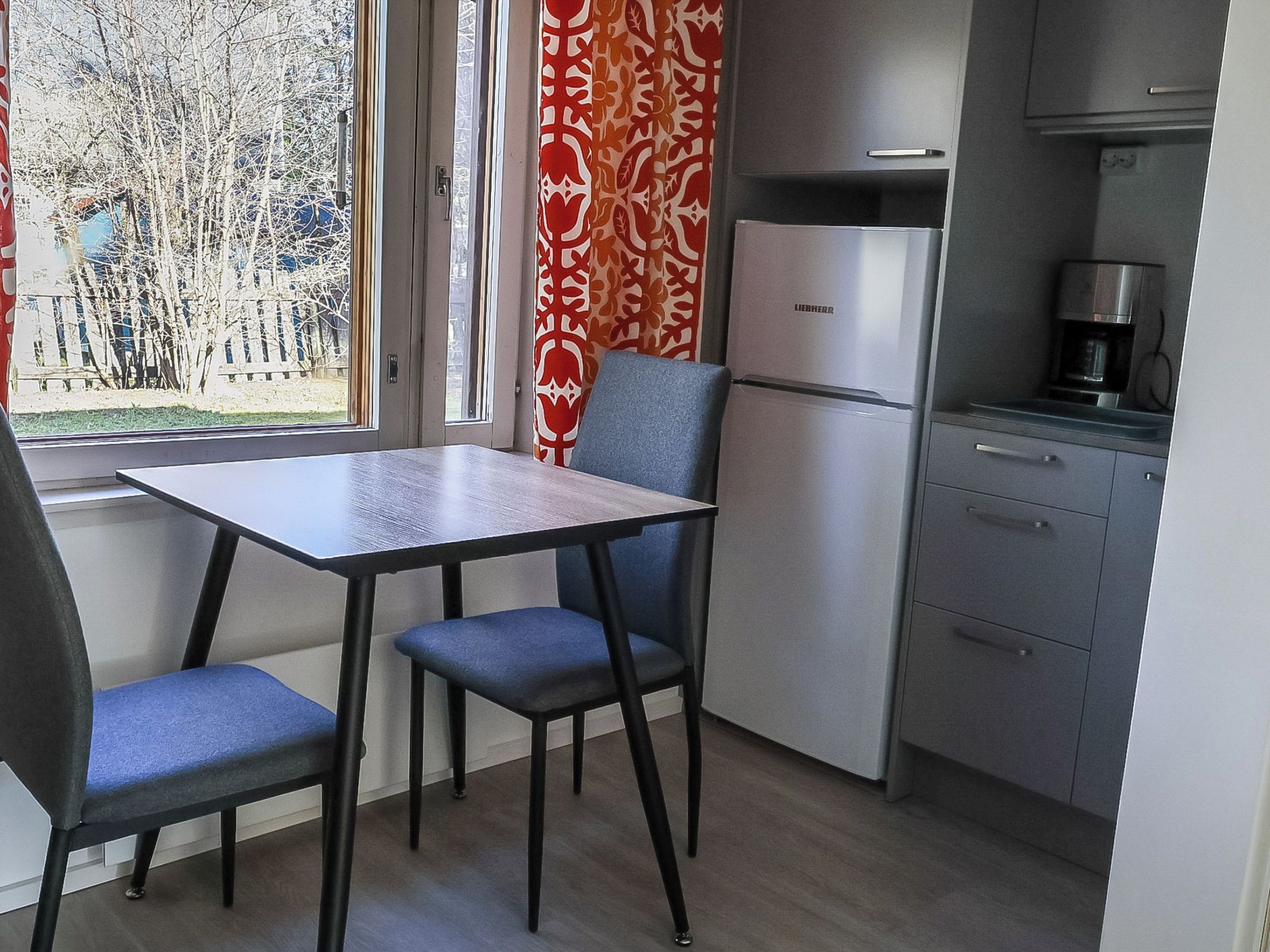 Pieni, käytännöllinen keittiö, jossa on pöytä ja tuolit, jääkaappi ja kahvinkeitin.